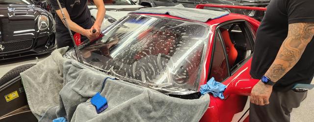 Installers applying film to the windshield of a red Ferrari F40