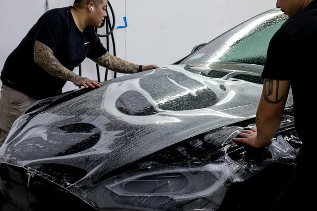 Two installers applying clear film to a black car's hood